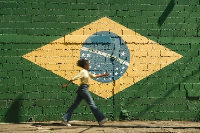 Street art of Brazilian flag painted on a wall with a woman walking past.
