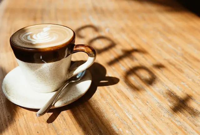 Cup of coffee on a table with the word cafe printed on the table.