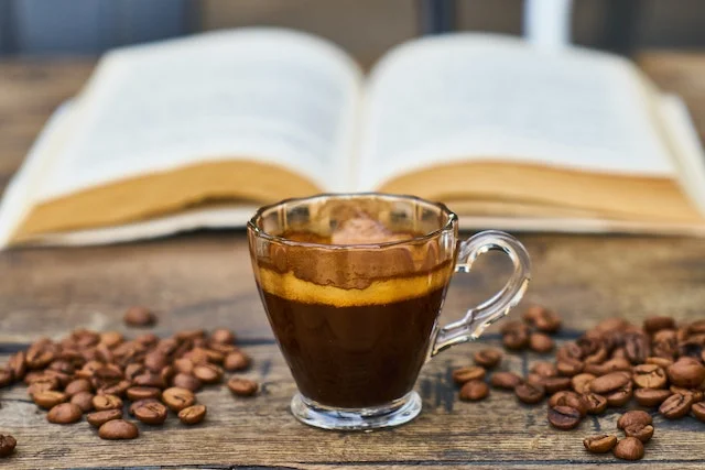 Cup of espresso with a crema in front of an open book with coffee beans either side of the cup.