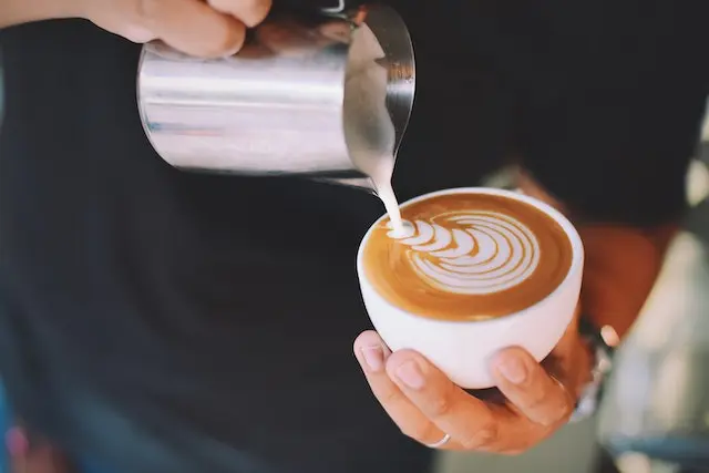 Steamed milk is poured into coffee showing how to make latte art.