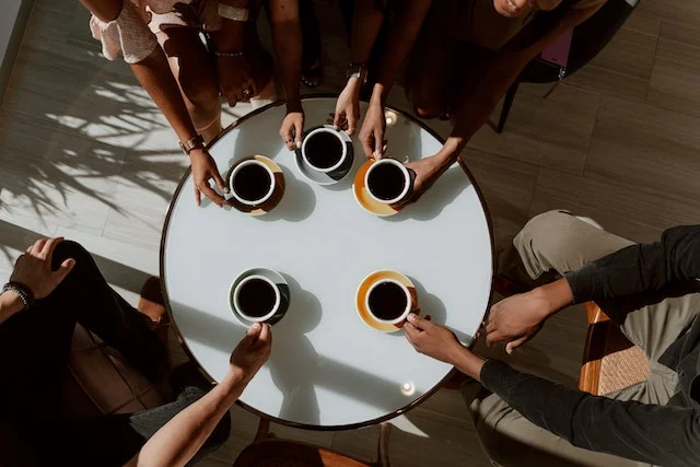 Hands around coffee cups around a table, a typical cafezinho social gathering.