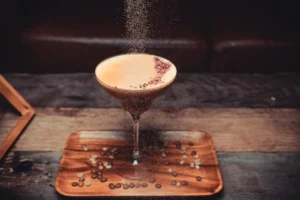 Coffee cocktail in a cocktail glass on a table with coffee beans scattered around it.