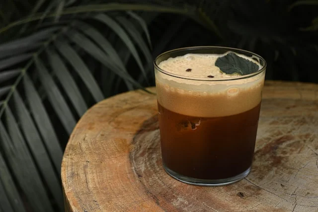 Dark cocktail in a glass on table, probably containing coffee cocktail.